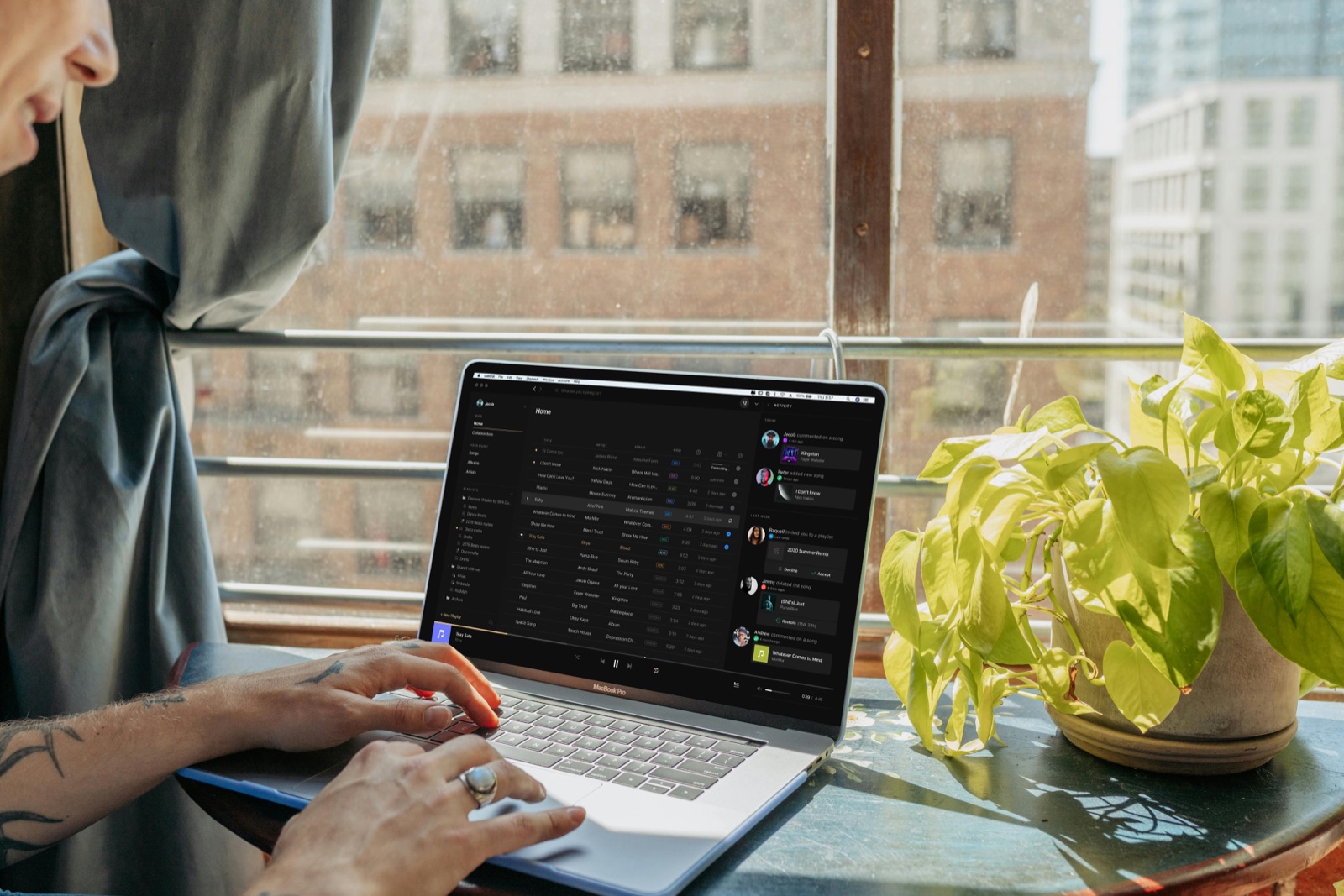 A composer browsing a music portfolio on a MacBook Pro by a sunny window